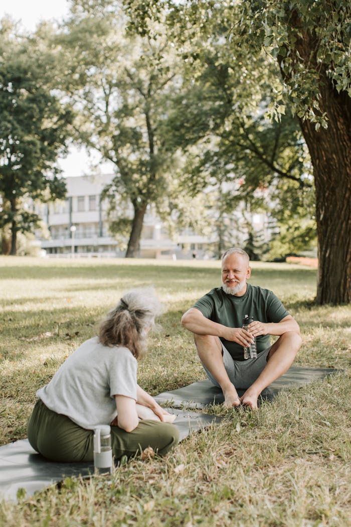Elderly couple enjoys a peaceful day outdoors on yoga mats in a park setting.